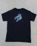 A black short-sleeve t-shirt with a glowing blue scorpion graphic on the chest, laid flat on a textured gray concrete surface.